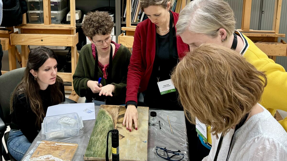 Five female researchers gathered around a table analyzing a varnish removal technique.