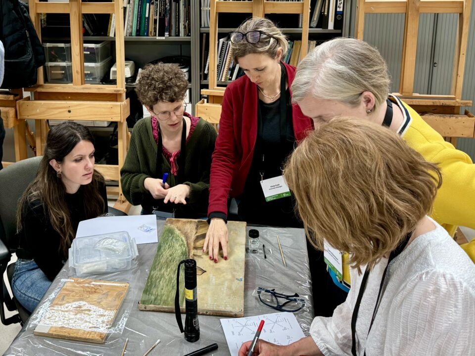 Five female researchers gathered around a table analyzing a varnish removal technique.